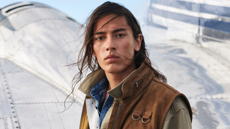 Banana Republic marketing image with a model wearing utility clothes standing in front of a plane.